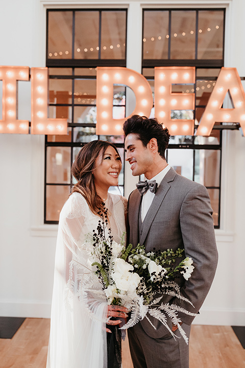 Building-177-Styled-Shoot-bride-and-groom-at-ceremony-space-bride-in-a-flowing-white-gown-with-short-sleeves-and-beading-detail-groom-in-a-grey-suit-with-a-grey-velvet-bow-tie