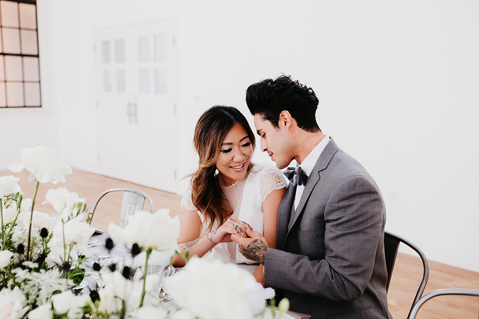 Building-177-Styled-Shoot-bride-and-groom-at-table-bride-in-a-flowing-white-gown-with-short-sleeves-and-beading-detail-groom-in-a-grey-suit-with-a-grey-velvet-bow-tie