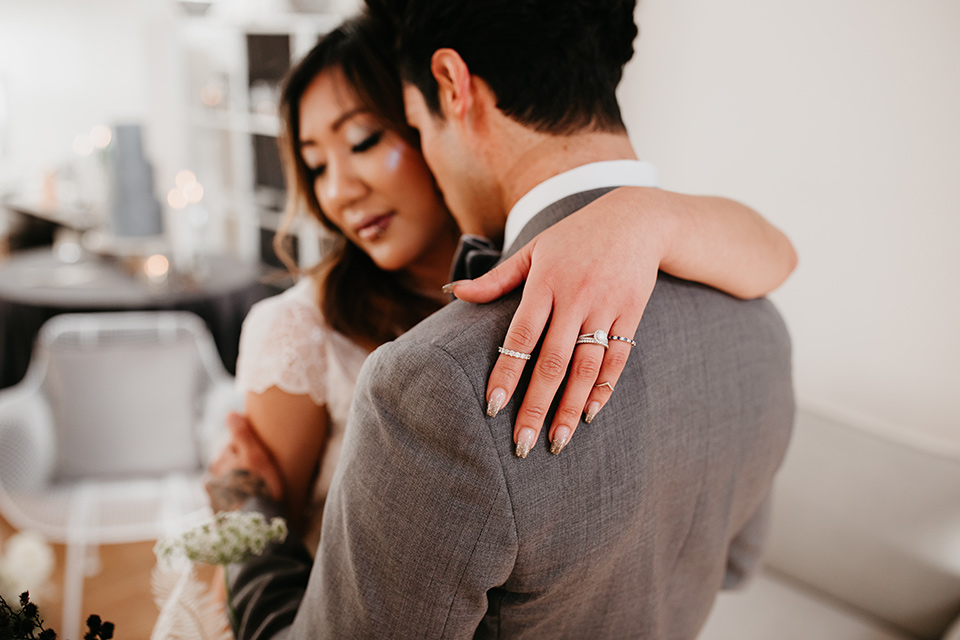 Building-177-Styled-Shoot-bride-and-groom-embrace-bride-in-a-flowing-white-gown-with-short-sleeves-and-beading-detail-groom-in-a-grey-suit-with-a-grey-velvet-bow-tie