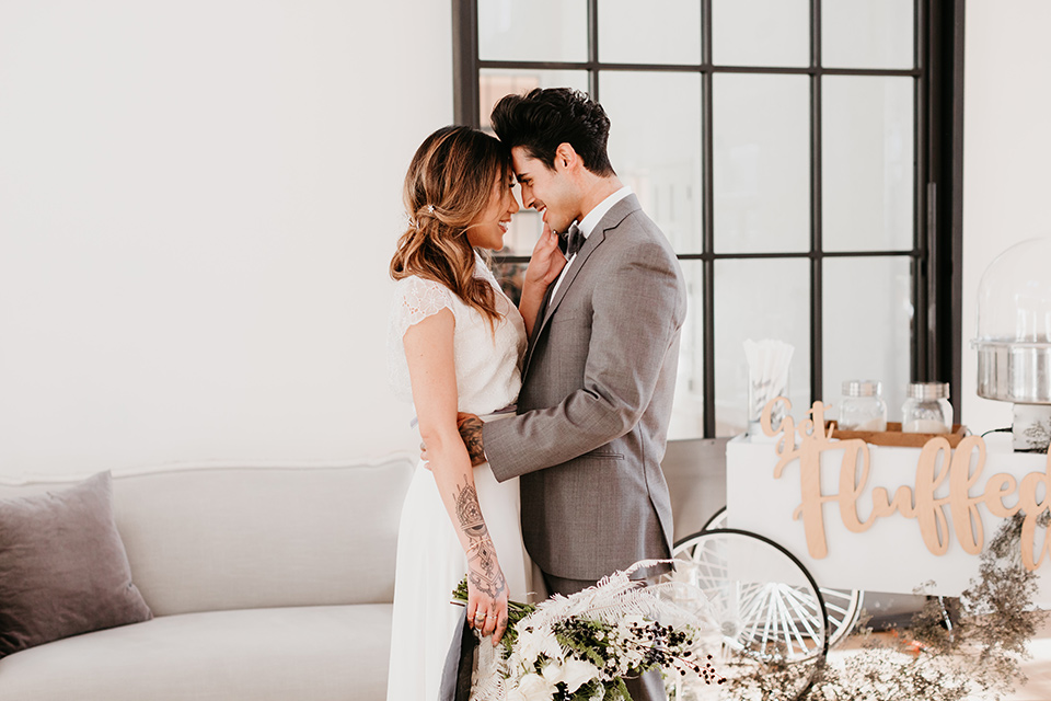 Building-177-Styled-Shoot-bride-and-groom-touching-heads-bride-in-a-flowing-white-gown-with-short-sleeves-and-beading-detail-groom-in-a-grey-suit-with-a-grey-velvet-bow-tie