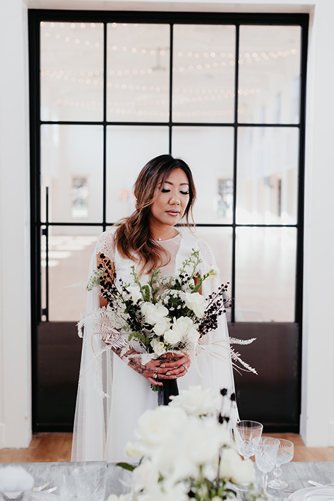 Building-177-Styled-Shoot-bride-looking-at-flowers-bride-in-a-flowing-white-gown-with-short-sleeves-and-beading-detail