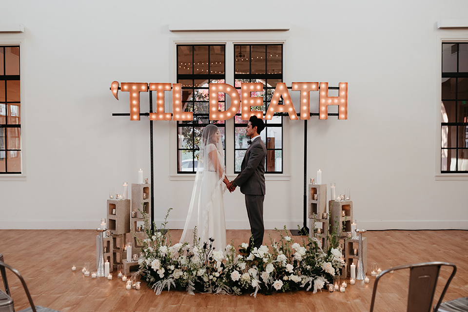 Building-177-Styled-Shoot-ceremony-space-decor-bride-in-a-flowing-white-gown-with-short-sleeves-and-beading-detail-groom-in-a-grey-suit-with-a-grey-velvet-bow-tie