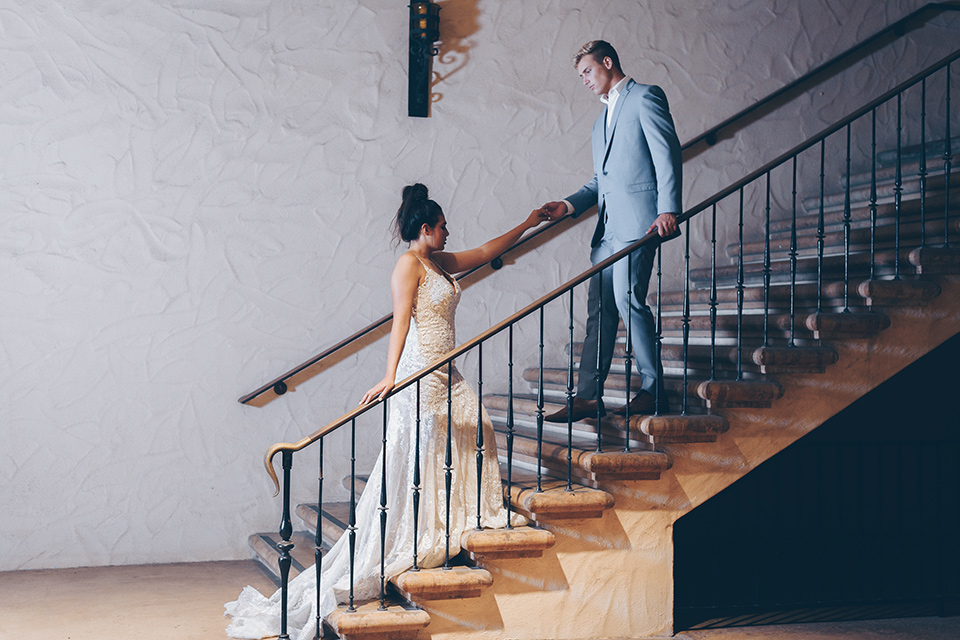  bride and groom on steps bride in a lace form fitting gown with thin straps groom in a light blue suit