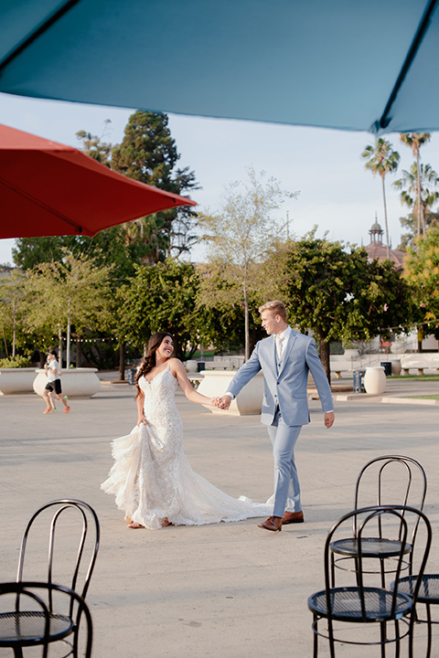  bride and groom walking away bride in a form fitting lace gown with thin straps groom in a light blue suit and looking in each others eye