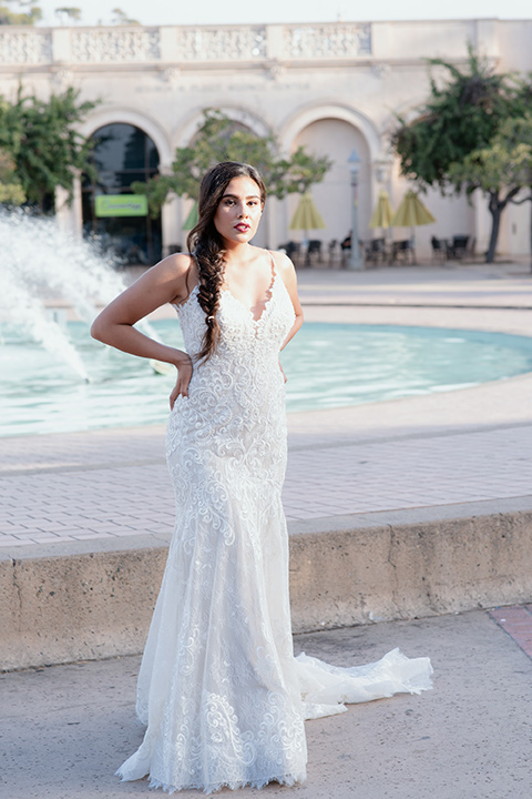 bride by fountain in a form-fitting lace gown with thin straps