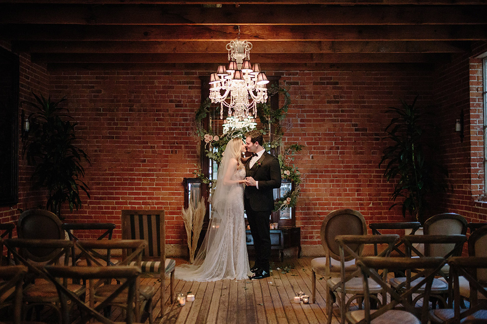 Carondelet-House-wedding-bride-and-groom-at-ceremony-bride-in-a-lace-gown-with-an-illusion-neckline-and-thin-straps-groom-in-a-traditional-black-tuxedo-with-a-black-bow-tie