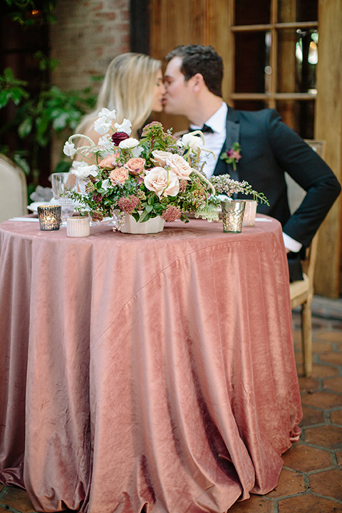 Carondelet-House-wedding-bride-and-groom-at-sweetheart-table-bride-and-groom-at-bride-in-a-lace-gown-with-an-illusion-neckline-and-thin-straps-groom-in-a-traditional-black-tuxedo-with-a-black-bow-tie