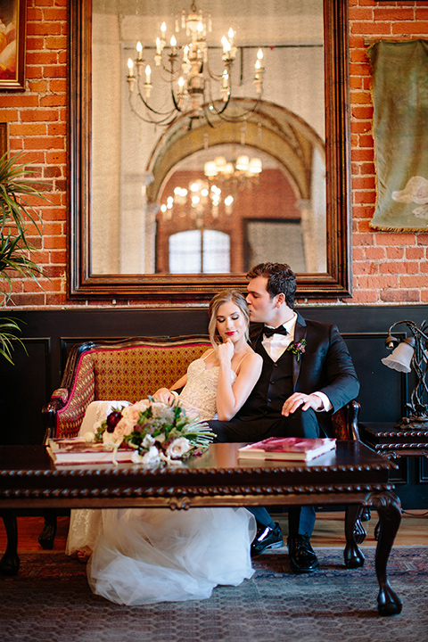 Carondelet-House-wedding-bride-and-groom-on-couch-bride-and-groom-at-bride-in-a-lace-gown-with-an-illusion-neckline-and-thin-straps-groom-in-a-traditional-black-tuxedo-with-a-black-bow-tie