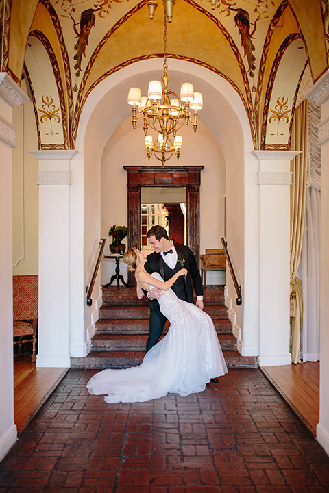 Carondelet-House-wedding-groom-dipping-bride-at-bride-in-a-lace-gown-with-an-illusion-neckline-and-thin-straps-groom-in-a-traditional-black-tuxedo-with-a-black-bow-tie