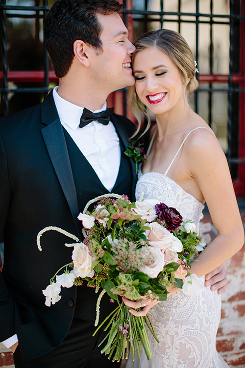 Carondelet-House-wedding-groom-kissing-bride-on-forehead-bride-in-a-lace-gown-with-an-illusion-neckline-and-thin-straps-groom-in-a-traditional-black-tuxedo-with-a-black-bow-tie