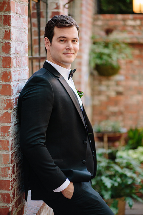 Carondelet-House-wedding-groom-leaning-on-wall-in-a-traditional-black-tuxedo-with-a-black-bow-tie