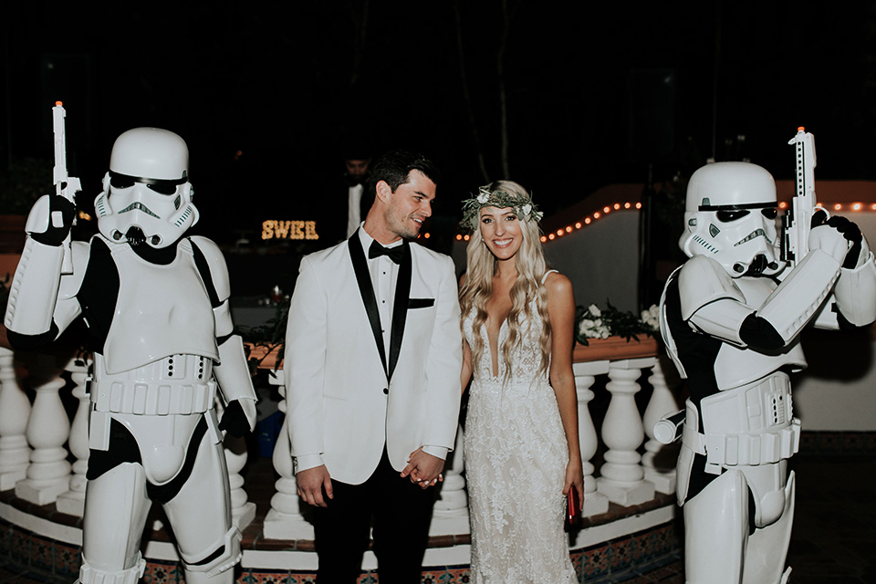 rancho-las-lomas-real-wedding-bride-and-groom-with-stormtroopers-the-bride-is-in-a-lace-long-gown-with-a-deep-v-and-straps-and-the-groom-is-in-a-white-shawl-lapel-tuxedo-with-black-pants-and-a-black-bow-tie