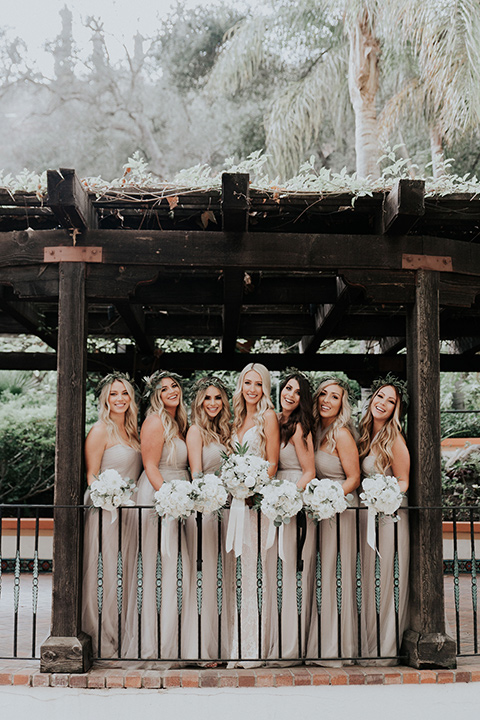 rancho-las-lomas-real-wedding-bridesmaids-under-wood-awning-the-bride-in-a-lace-white-gown-with-a-straps-and-a-deep-v-neckline-the-bridesmaids-in-a-taupe-long-gowns