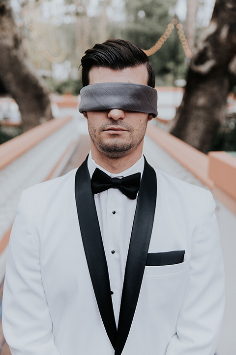 rancho-las-lomas-real-wedding-groom-with-cover-on-eyes-in-a-white-shawl-lapel-tuxedo-with-black-pants-and-a-black-bow-tie