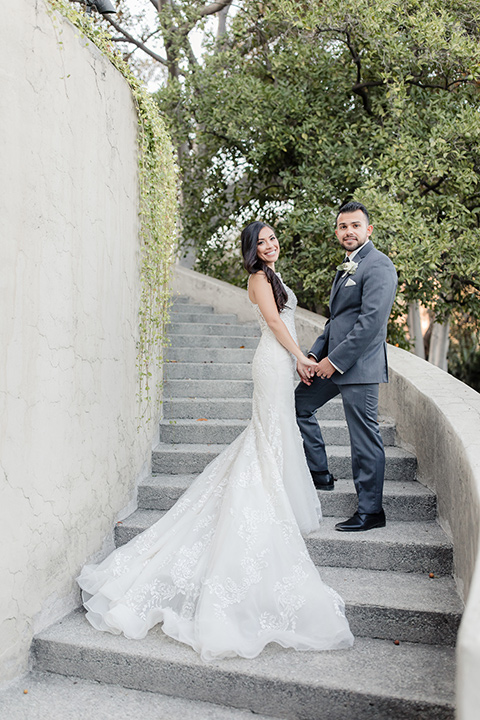 kellogg-house-pomona-wedding-bride-and-groom-on-steps-bride-in-a-lace-white-gown-with-a-high-neckline-and-a-mermaid-style-skirt-and-the-groom-in-a-dark-grey-tuxedo-with-a-black-bow-tie