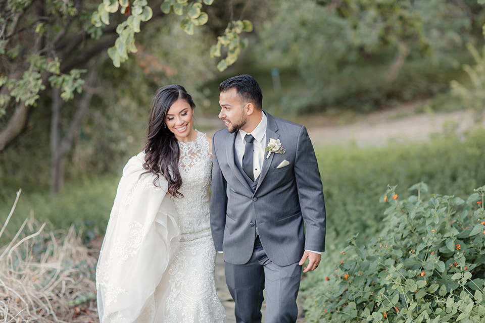 kellogg-house-pomona-wedding-bride-and-groom-walking-the-bridesmaids-are-in-pink-toned-gowns-the-groomsmen-in-light-grey-suits-bride-in-a-mermaid-style-gown-with-a-high-neckline-and-the-groom-in-a-dark-grey-tuxedo