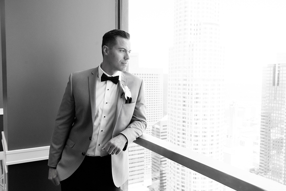 City-club-shoot-groom-looking-out-window-in-a-white-coat-with-black-pants