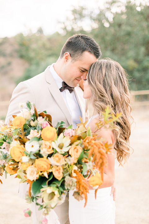 Claudia+Johns-meadow-elopement-bride-and-groom-touching-heads-bride-holding-florals-bride-in-a-two-toned-gown-with-a-light-pink-sjirt-and-a-white-silk-top-the-groom-is-in-a-tan-suit-with-a-deep-brown-bow-tie