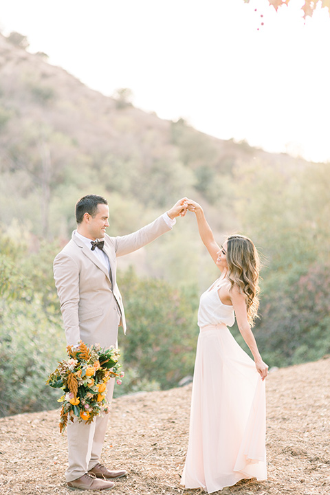 Claudia+Johns-meadow-elopement-bride-and-groom-twirling-bride-in-a-two-toned-gown-with-a-light-pink-sjirt-and-a-white-silk-top-the-groom-is-in-a-tan-suit-with-a-deep-brown-bow-tie