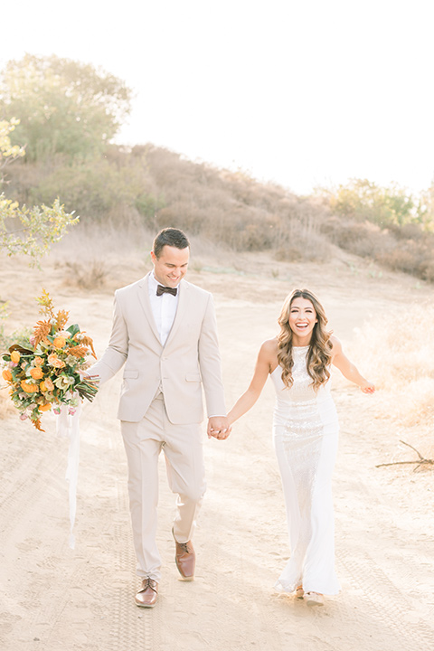 Claudia+Johns-meadow-elopement-bride-and-groom-walking-bride-in-a-two-toned-gown-with-a-light-pink-sjirt-and-a-white-silk-top-the-groom-is-in-a-tan-suit-with-a-deep-brown-bow-tie