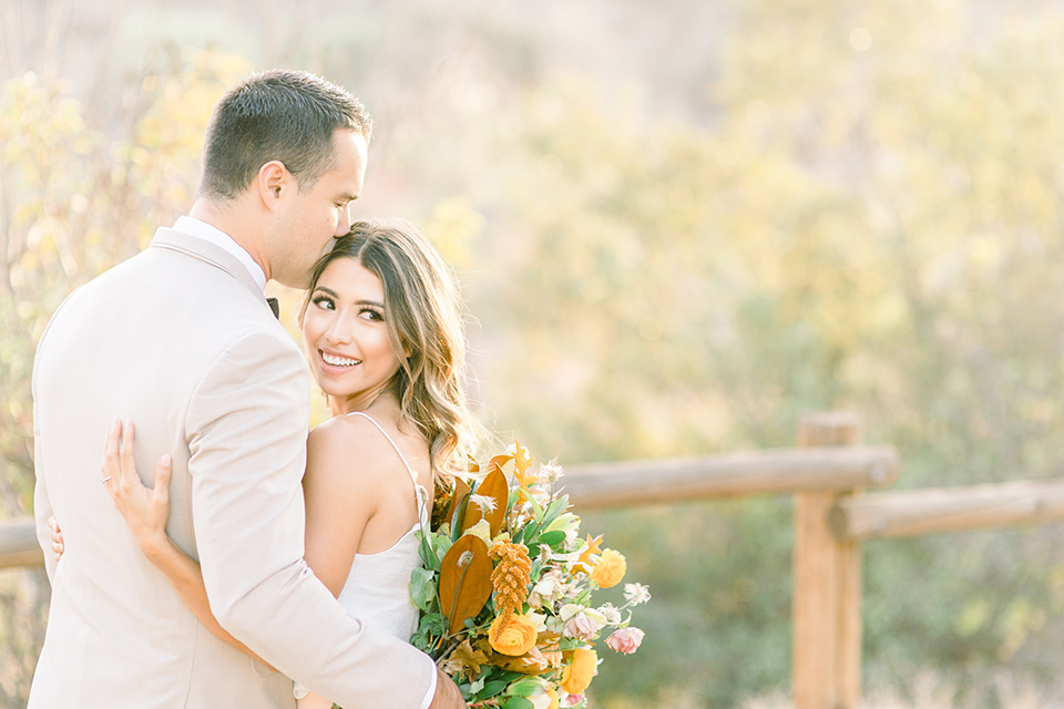 Claudia+Johns-meadow-elopement-bride-looking-at-camera-groom-looking-away-bride-in-a-blush-skirt-and-white-silk-top-the-groom-is-in-a-tan-suit-with-a-brown-bow-tie