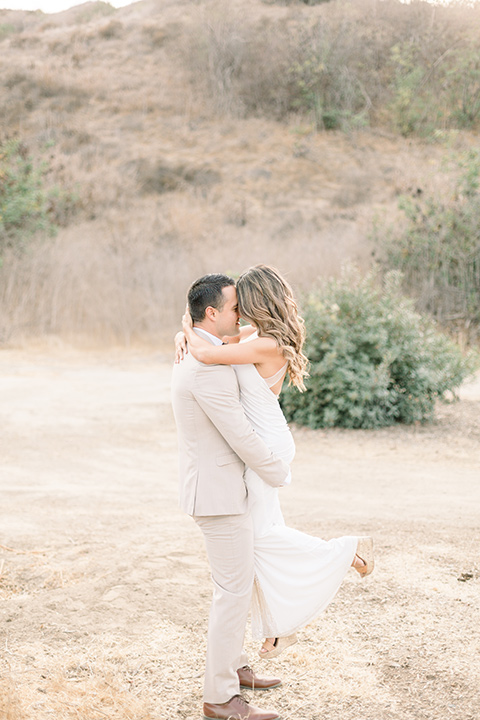 Claudia+Johns-meadow-elopement-groom-holding-up-bride-bride-in-a-two-toned-gown-with-a-blush-skirt-with-a-white-silk-top-and-the-groom-in-a-tan-suit-with-a-deep-brow-bow-tie