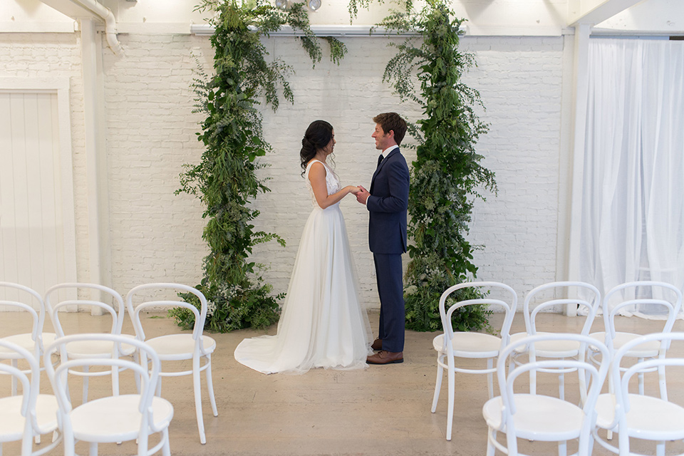 Cooks-Chapel-Shoot-bride-and-groom-at-ceremony-bride-is-in-a-white-flowing-gown-with-a-deep-v-neckline-groom-is-in-a-dark-blue-suit-with-a-navy-long-tie-and-brown-shoes