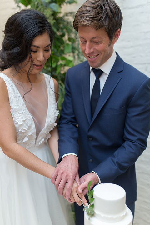 ”Cooks-Chapel-Shoot-bride-and-groom-cutting-cake-bride-in-a-soft-flowing-gown-with-a-plunging-neckline-while-the-groom-is-in-a-dark-blue-suit-with-a-navy-long-tie-and-brown-shoes"