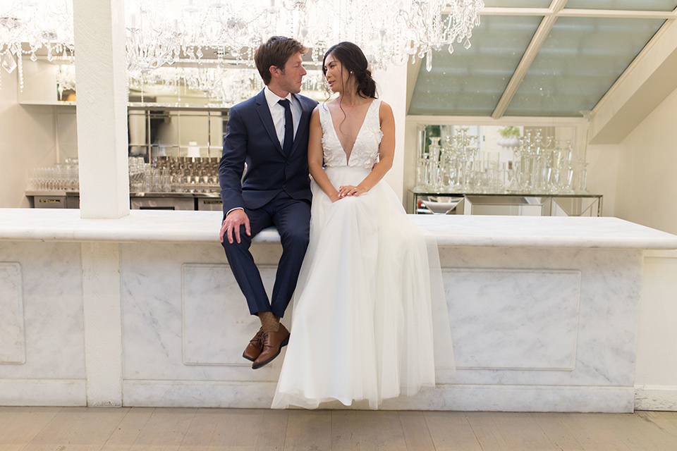 Cooks-Chapel-Shoot-bride-and-groom-on-bar-bride-is-in-a-white-flowing-gown-with-a-deep-v-neckline-groom-is-in-a-dark-blue-suit-with-a-navy-long-tie-and-brown-shoes