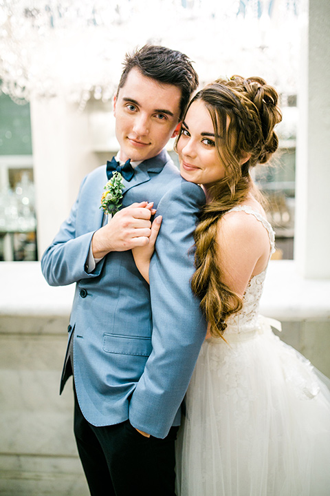 Wedding groom hugging the bride in a white ballgown with a lace bodice and straps. The groom is wearing a light blue coat with a dark blue vest in the anaheim packing house