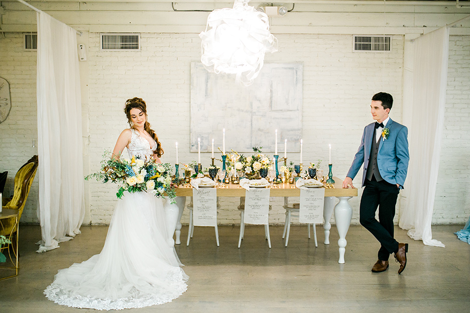 Wedding bride and groom on either side of the table with the bride in a white ballgown with a lace bodice and the groom in a light blue coats