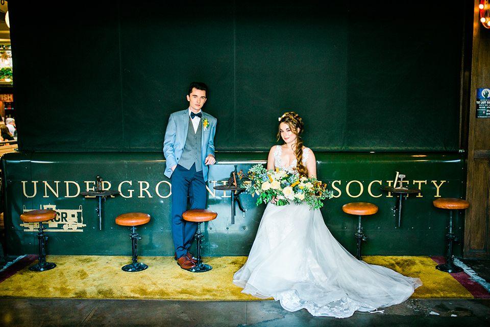 Cooks-Chapel-Wedding-bride-and-groom-sitting-at-bar-the-bride-in-a-white-ballgown-with-a-lace-bodice-and-straps-the-groom-is-in-a-light-blue-coat-with-adark-blue-vest-and-pants-with-a-dark-blue-bow-tie