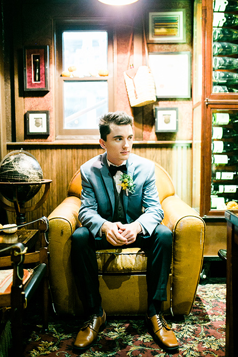  wedding groom sitting in a chair in a light blue coat with a dark blue bow tie