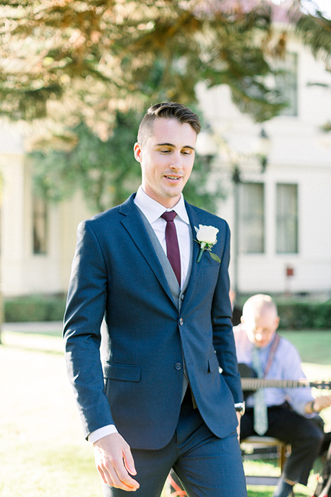 red-barn-wedding-groom-walking-down-ceremony-aisle-groom-in-a-blue-suit-with-grey-vest-and-burgundy-tie