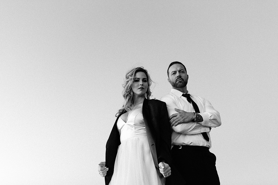 Bohemian-Desert-Shoot-bride-and-groom-from-low-angle-bride-in-a-formfitting-gown-with-lace-detailing-and-a-sweetheart-neckline-groom-in-a-burgundy-shawl-lapel-tuxedo-with-a-black-long-tie