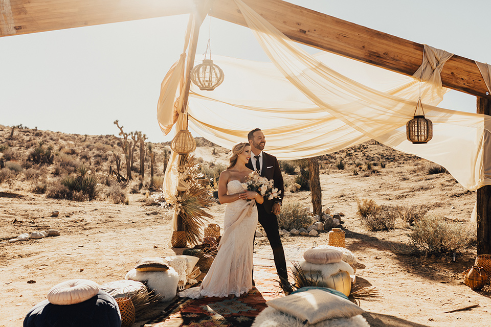 Bohemian-Desert-Shoot-bride-and-groom-in-ceremony-space-bride-in-a-formfitting-gown-with-lace-detailing-and-a-sweetheart-neckline-groom-in-a-burgundy-shawl-lapel-tuxedo-with-a-black-long-tie