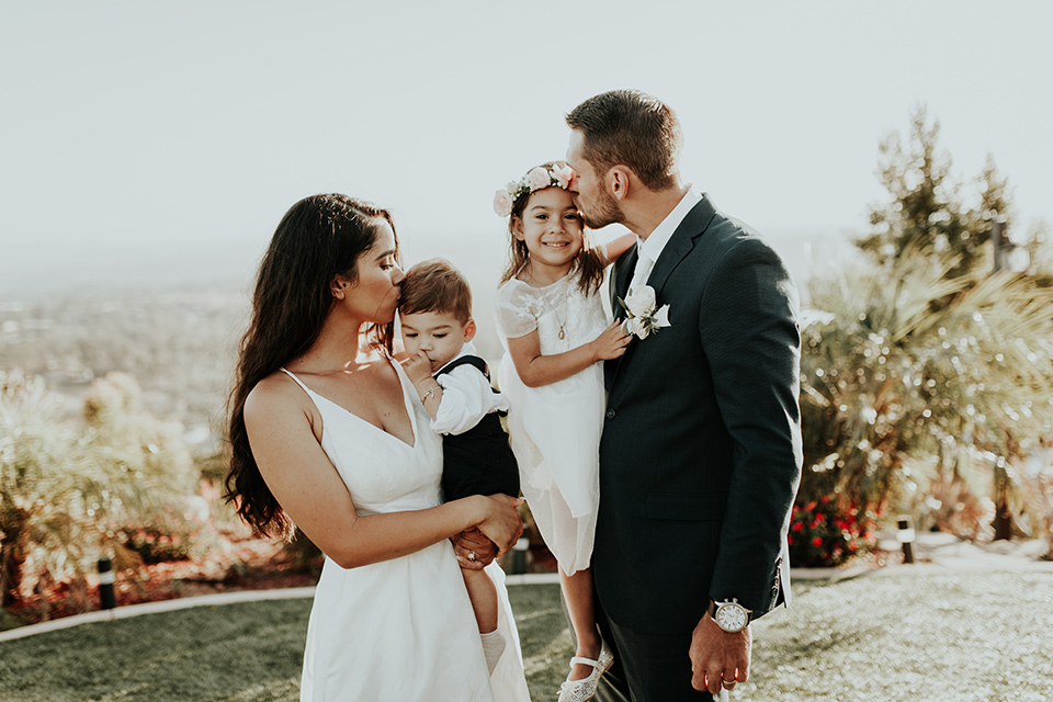 Dragon-point-villa-wedding-bride-and-groom-kissing-their-children-bride-in-a-white-ballgown-with-pockets-and-thin-straps-groom-in-a-black-suit-with-a-white-tie