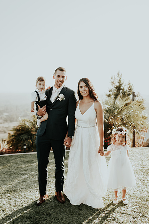 Dragon-point-villa-wedding-bride-and-groom-smiling-with-kids-bride-in-a-white-ball-gown-with-sleeves-and-straps-groom-in-a-slim-black-suit-with-a-white-tie