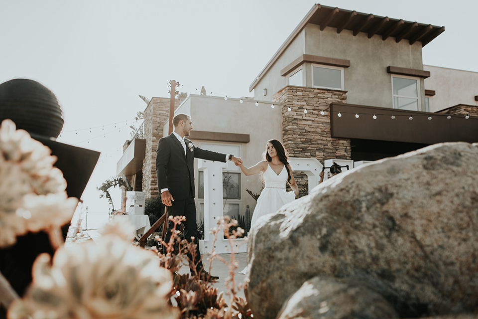 Dragon-point-villa-wedding-bride-and-groom-walking-by-building-bride-in-a-white-ballgown-with-pockets-and-thin-straps-groom-in-a-black-suit-with-a-white-tie