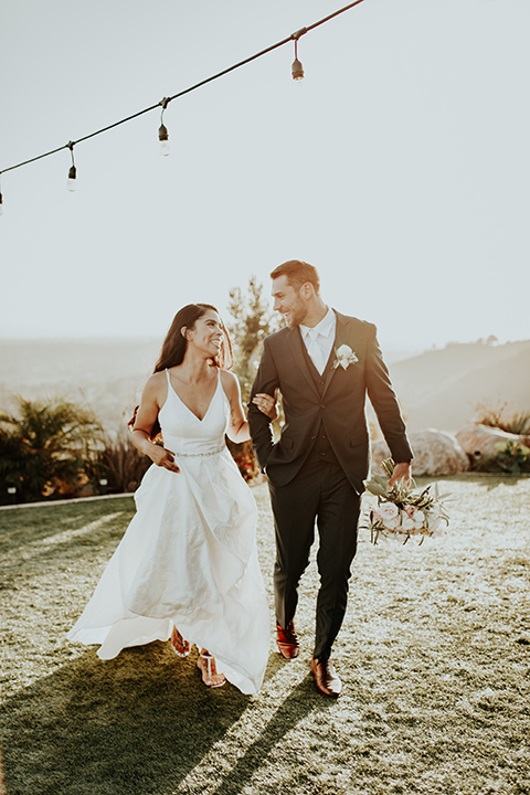 Dragon-point-villa-wedding-bride-and-groom-walking-on-grass-bride-in-a-white-ball-gown-with-pockets-and-thin-straps-groom-in-a-black-suit-and-white-tie