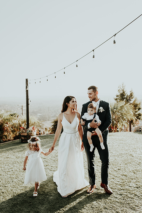 Dragon-point-villa-wedding-bride-and-groom-walking-with-the-kids-bride-in-a-white-ball-gown-with-pockets-and-thin-straps-groom-in-a-black-suit-and-white-tie