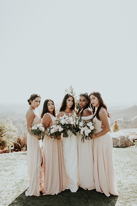 Dragon-point-villa-wedding-bridesmaids-looking-at-camera-bride-in-a-white-ball-gown-with-pockets-and-bridesmaids-in-light-pink-long-dresses