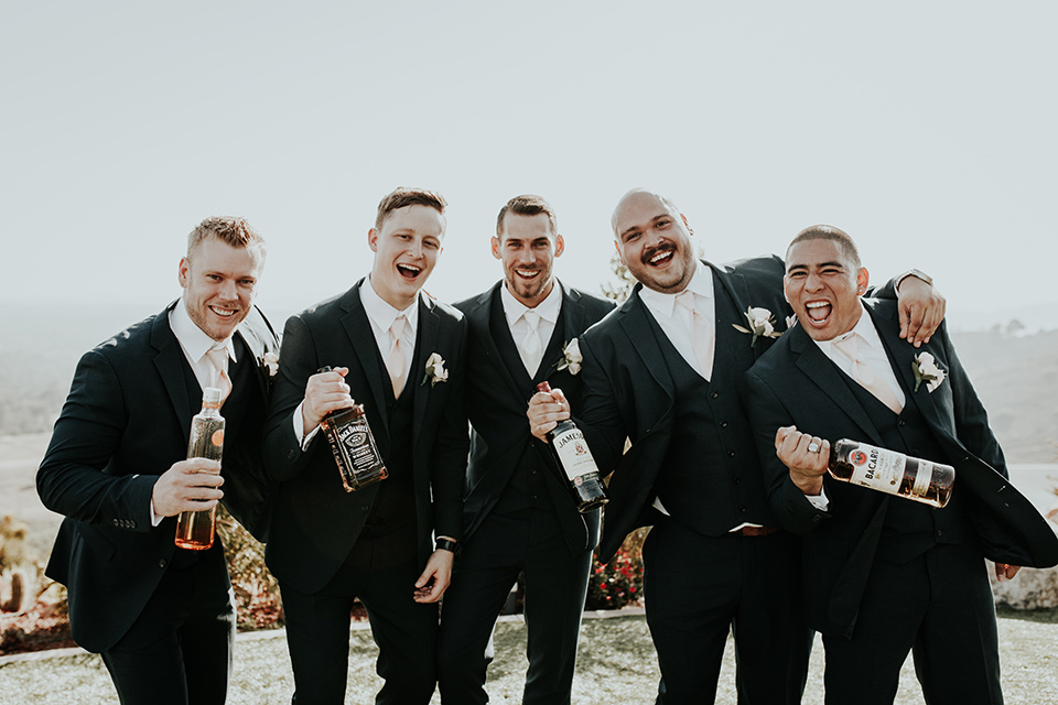 Dragon-point-villa-wedding-groomsmen-holding-alcohol-bottles-groom-and-groomsmen-in-black-suits-groomsmen-with-pink-ties-groom-with-a-white-tie