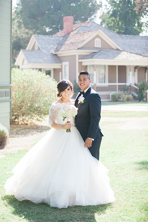 Elements-Venue-presents-wedding-bride-and-groom-smiling-at-camera-bride-is-in-a-layered-tulle-ball-gown-with-a-high-neckline-and-quarter-sleeves-groom-in-a-navy-blue-shawl-lapel-tuxedo-with-a-black-bow-tie