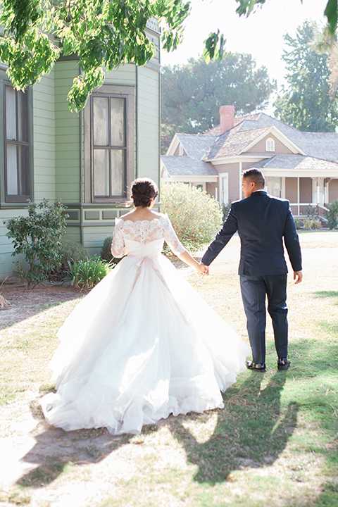 ”Elements-Venue-presents-wedding-bride-and-groom-walking-away-bride-is-in-a-layered-tulle-ball-gown-with-a-high-neckline-and-quarter-sleeves-groom-in-a-navy-blue-shawl-lapel-tuxedo-with-a-black-bow-tie"