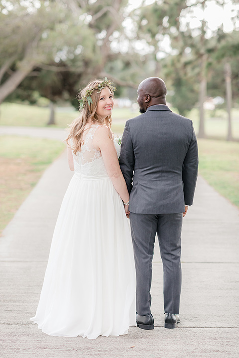 Los-Verdes-Golf-Course-Wedding-bride-looking-over-shoulder-and-groom-holding-hands-bride-in-a-white-gown-with-cap-sleeves-groom-in-a-charcoal-tuxedo-with-a-black-tie