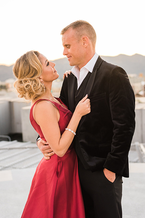 bride in a red evening gown with a plunging neckline and hair in a bun, groom in a black velvet tuxedo and black bow tie