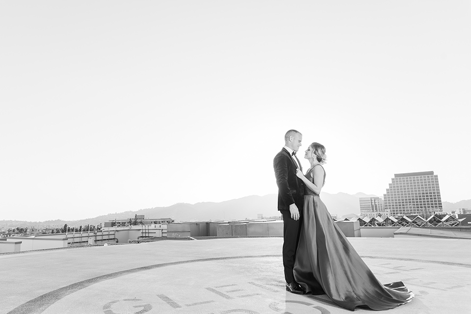  bride in a red evening gown with a plunging neckline and hair in a bun, groom in a black velvet tuxedo and black bow tie 