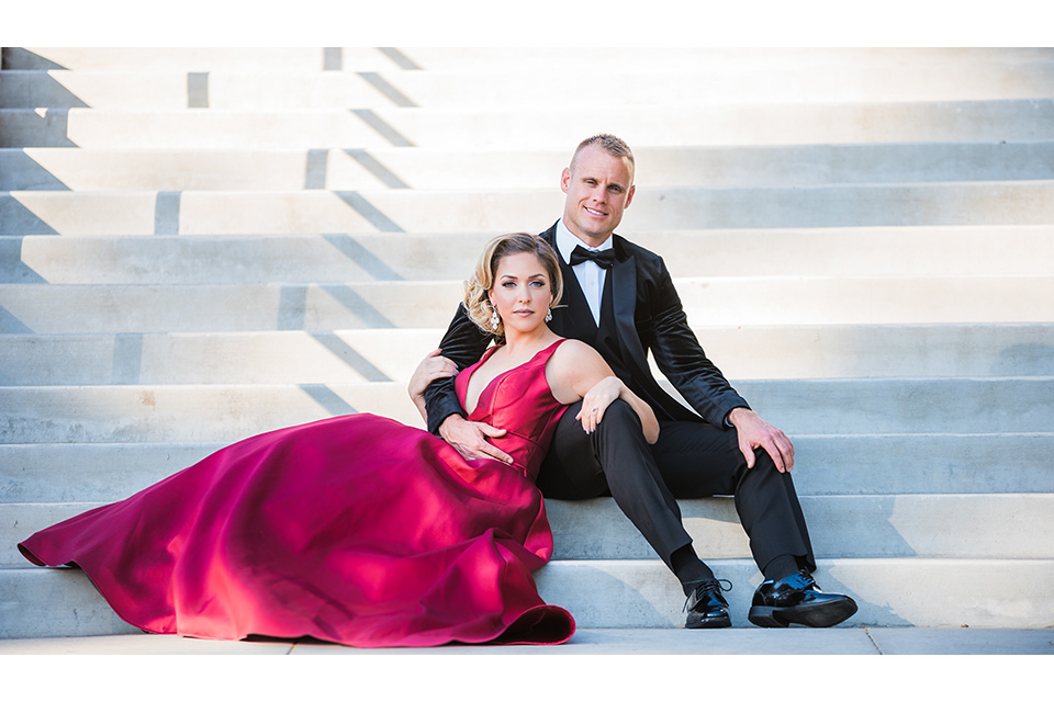  bride in a red evening gown with a plunging neckline and hair in a bun, groom in a black velvet tuxedo and black bow tie 