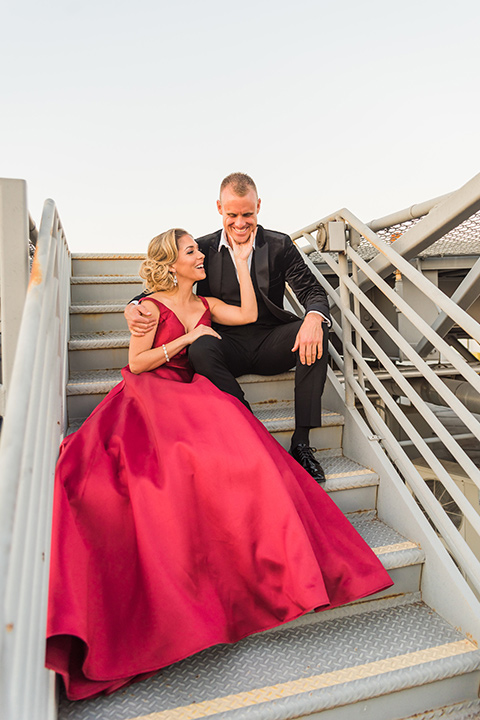  bride in a red evening gown with a plunging neckline and hair in a bun, groom in a black velvet tuxedo and black bow tie 